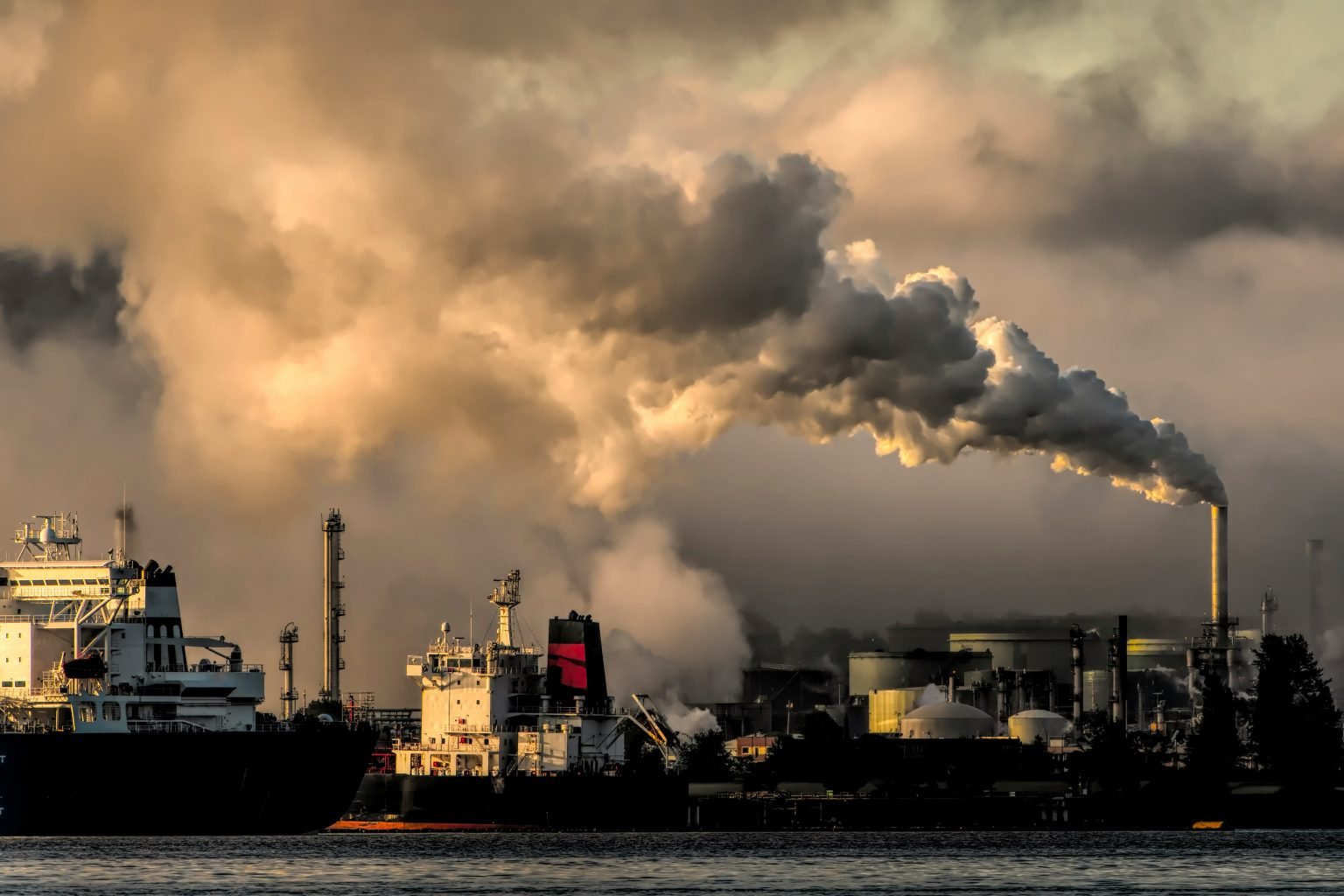 A picture of a container ship at port next to an exhaust pipe for gas into the atmosphere.