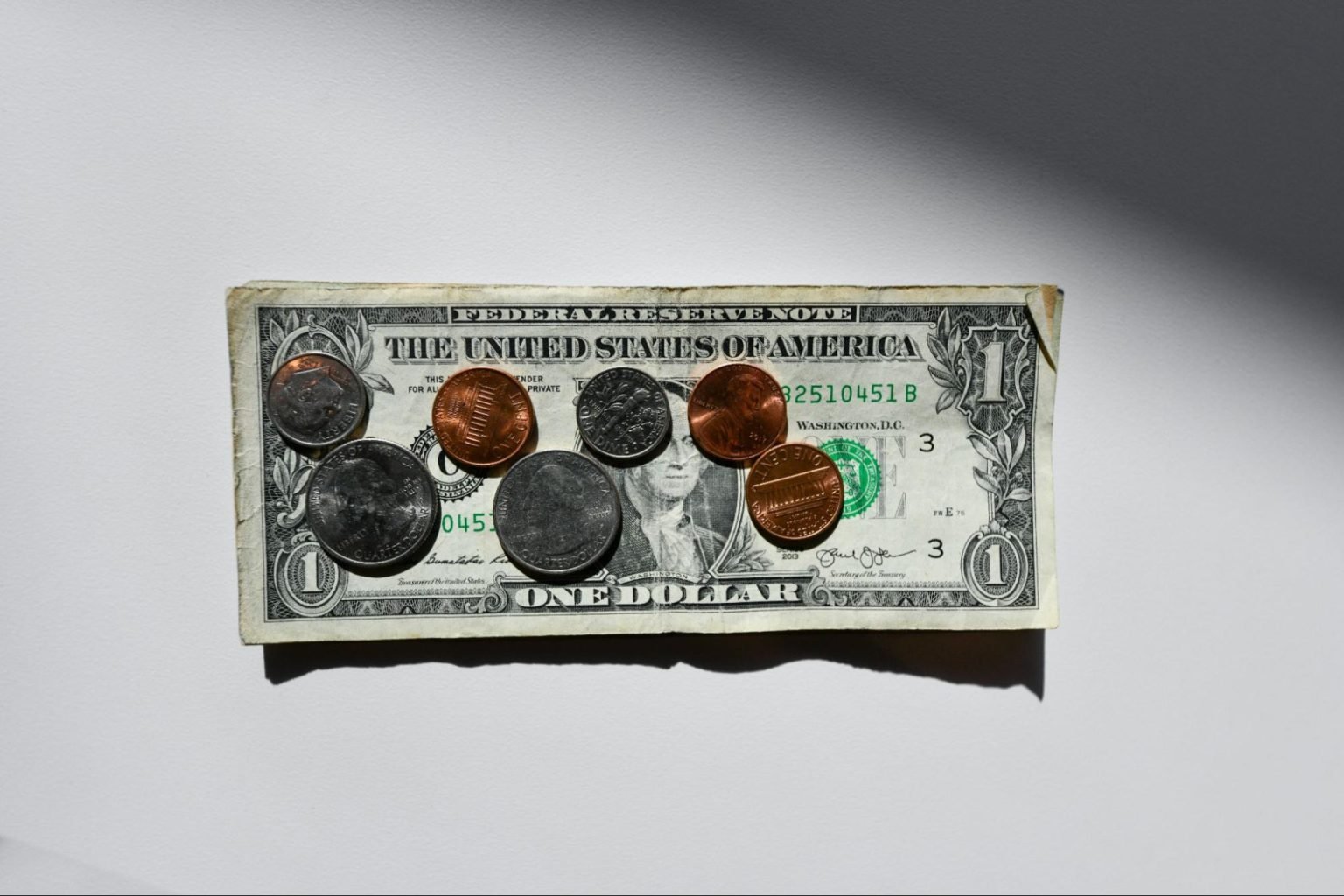 A dollar bill over a white background; on top of ir, a number of coins.